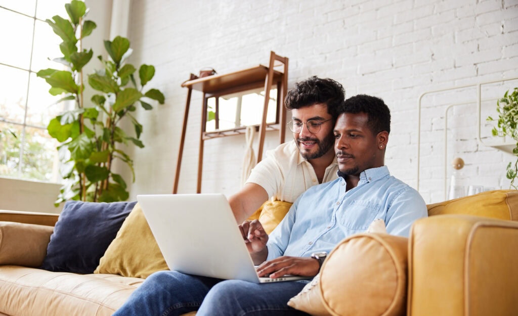 Smiling young gay working on a laptop in their living room